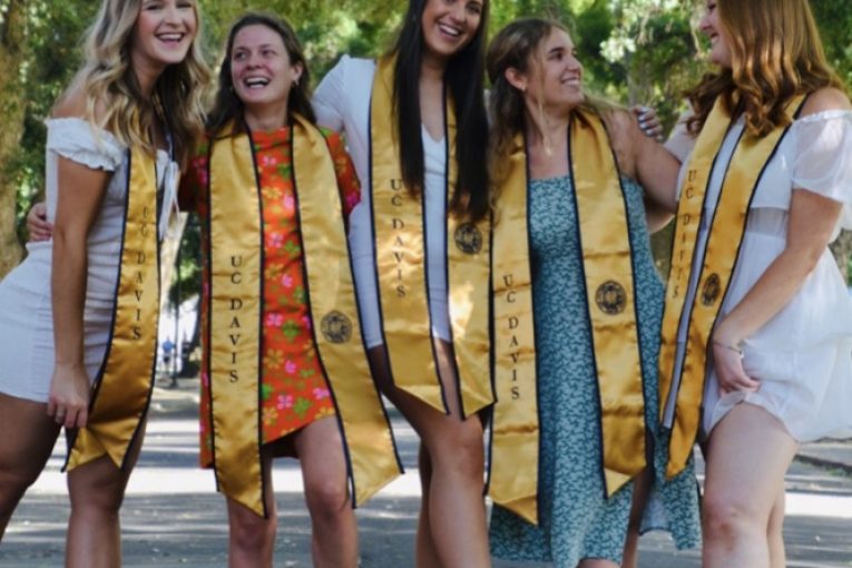 Graduate photo of 5 white women in dresses standing on the road.