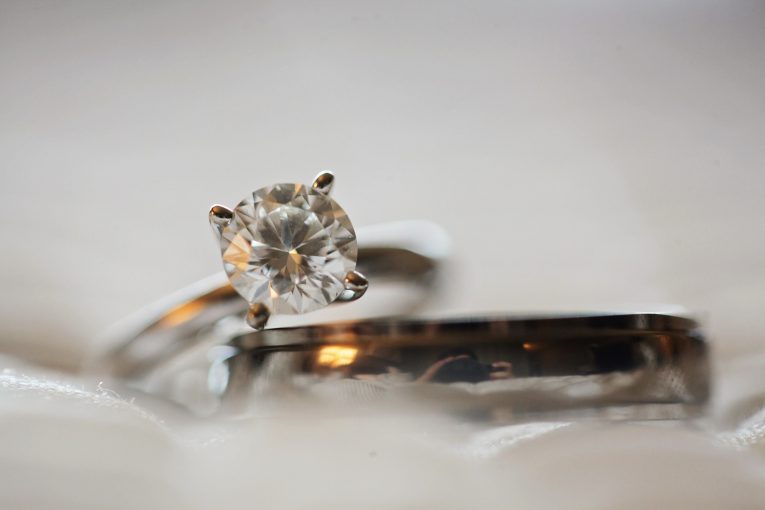 Two silver rings on a grey background, the top ring has a diamond mounted on it